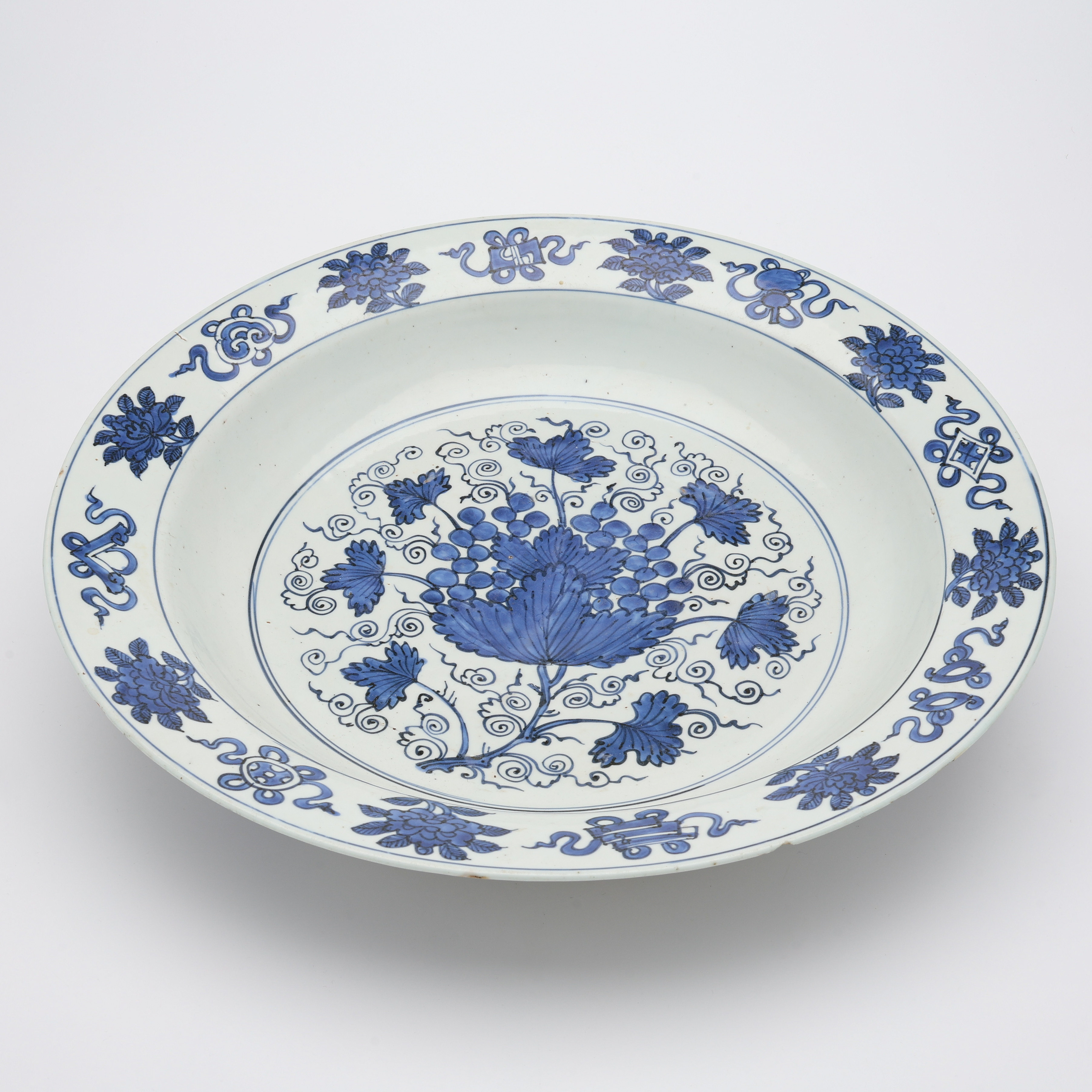 'GRAPES' CHARGER/ETT STORT SKÅLFAT, KINA. Troligen Jiajing (1522-1566). Porslin med måleri i koboltblått föreställande vinranka och bårder.