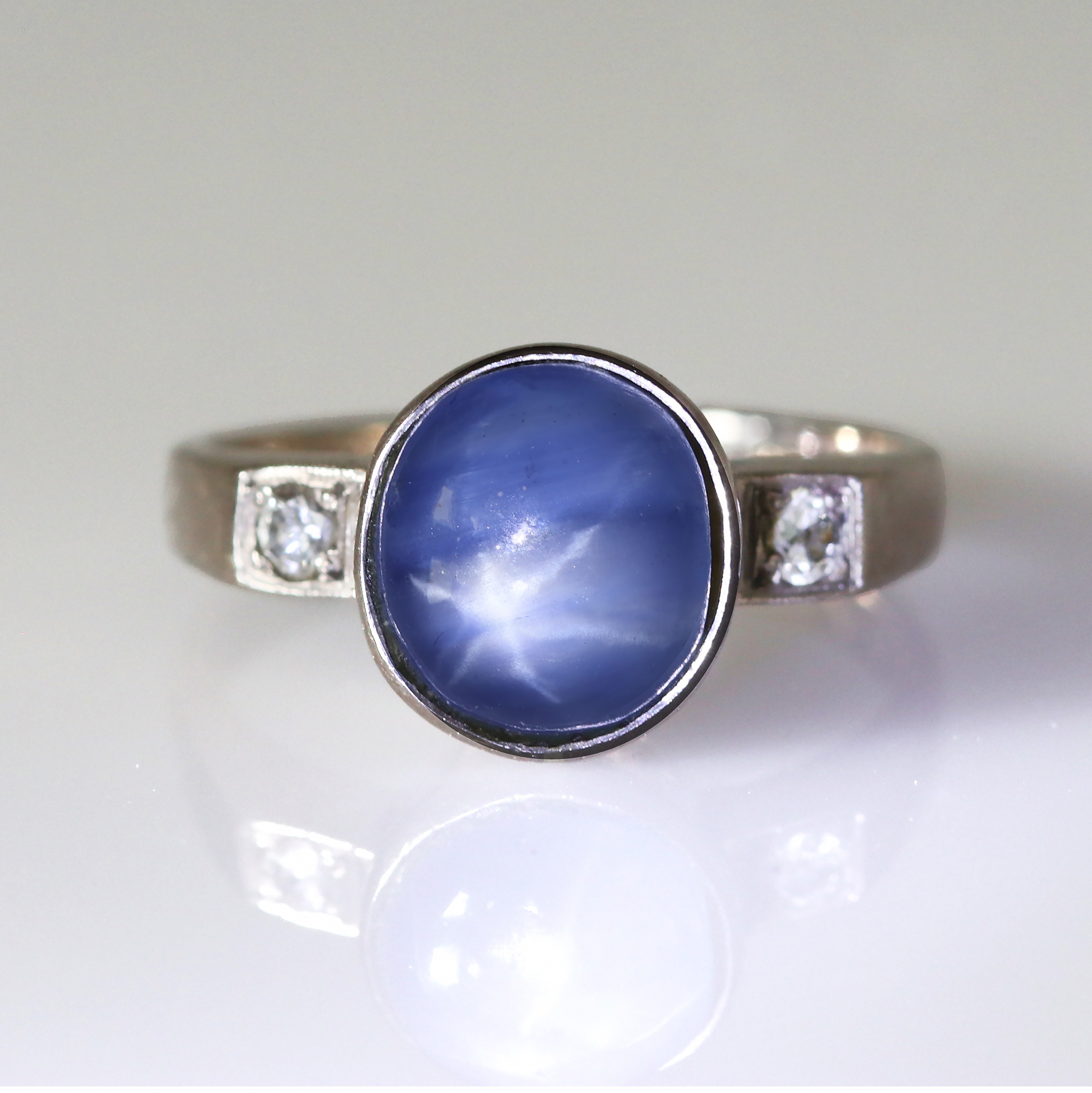 RING MED STJÄRNSAFIR. 18k vitguld med en gråblå cabochonslipad stjärnsafir och två små diamanter, totalvikt ca 4,6 gram.