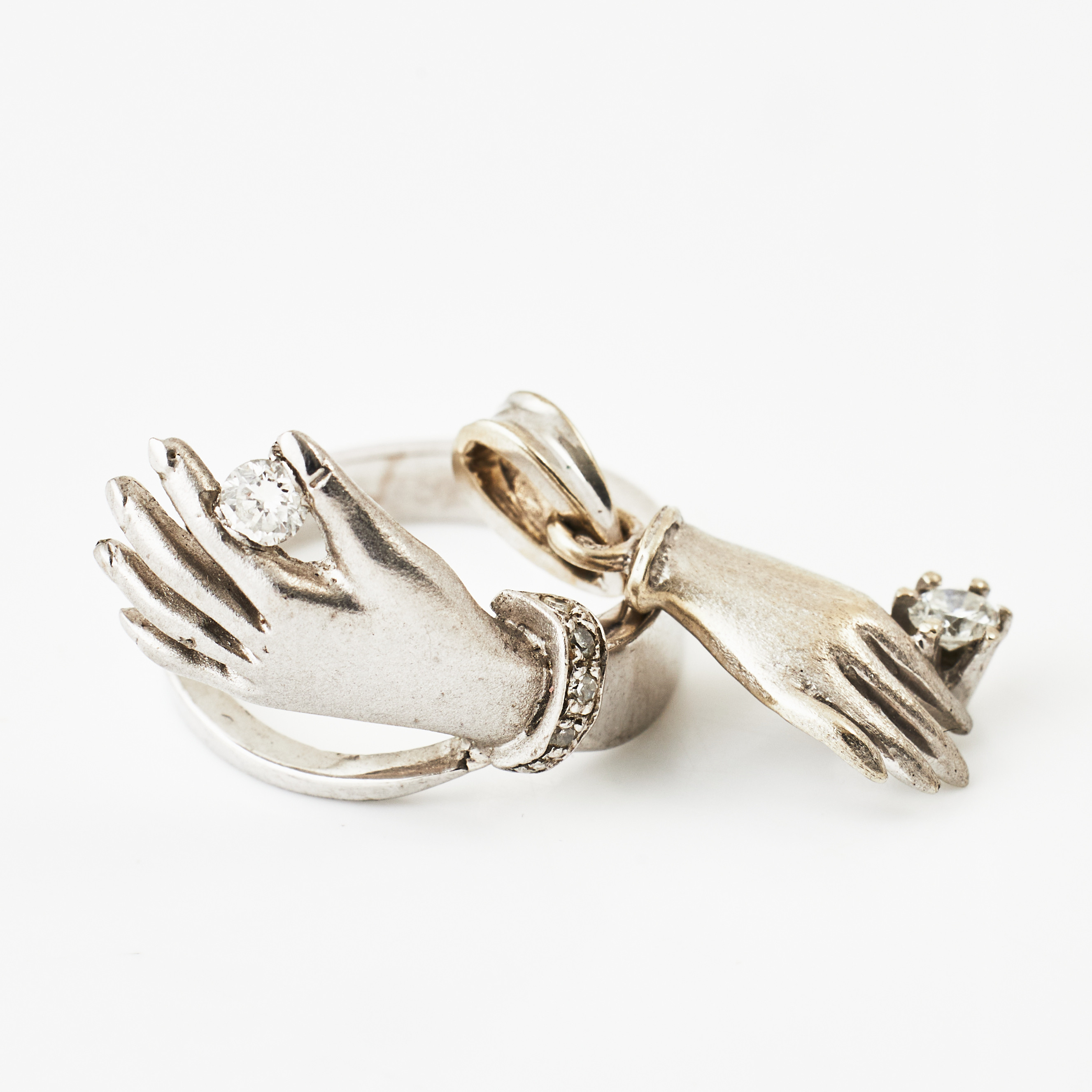 RING, 18 k satinerat- och blankslipat vitguld, i form av hand hållandes en briljant 0,10 ct., 4 små åttkantslipade diamanter på handled, Juvelerare Elof Olsson AB, Göteborg 1985, HÄNGE, 14 k vitguld, liknande, briljant ca 0,07 ct, utländsk stämpel.