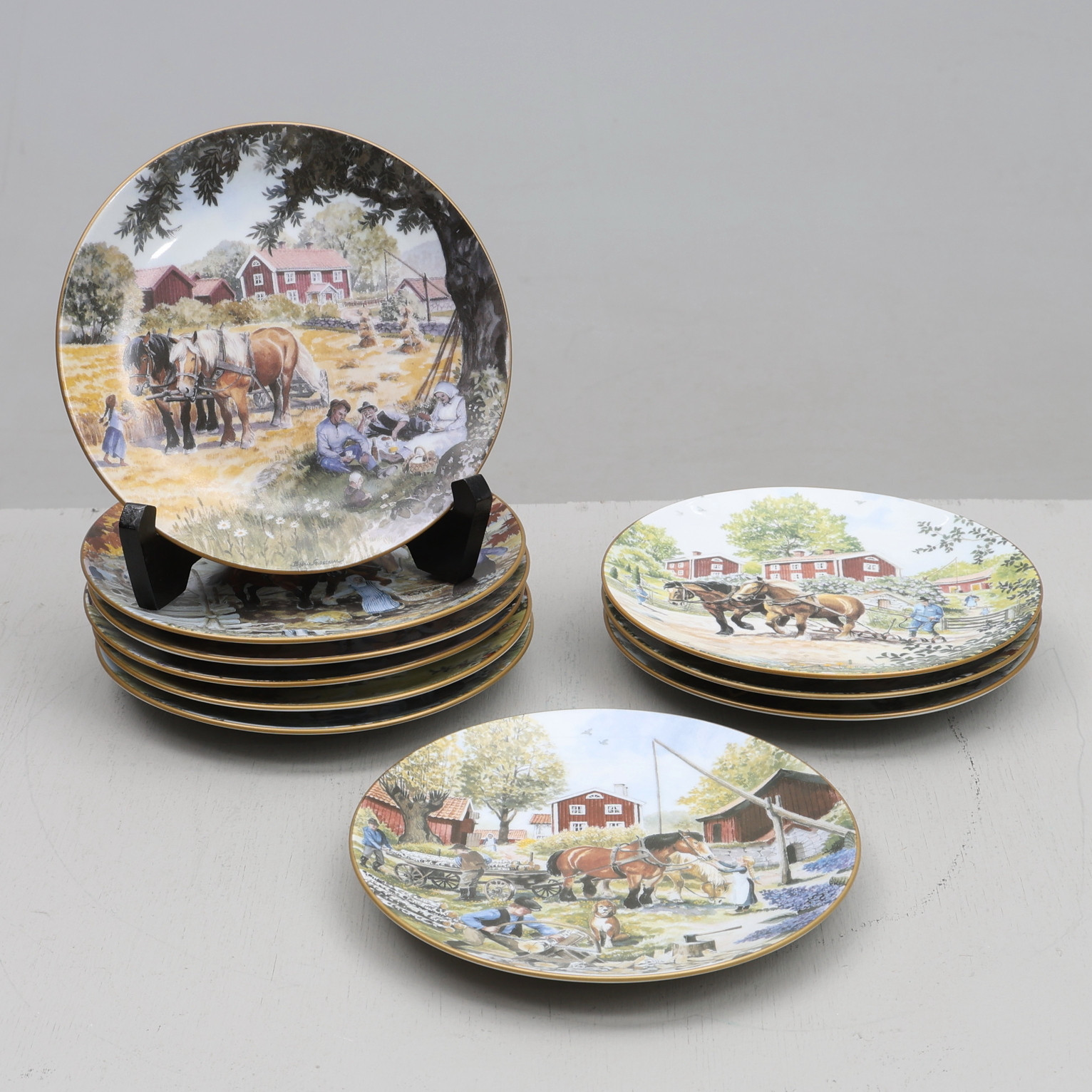 BJÖRN GIDSTAM. Samlartallrikar, 10 st, porslin, "Det svenska bondesamhället", Guldkroken, 1900-tal.