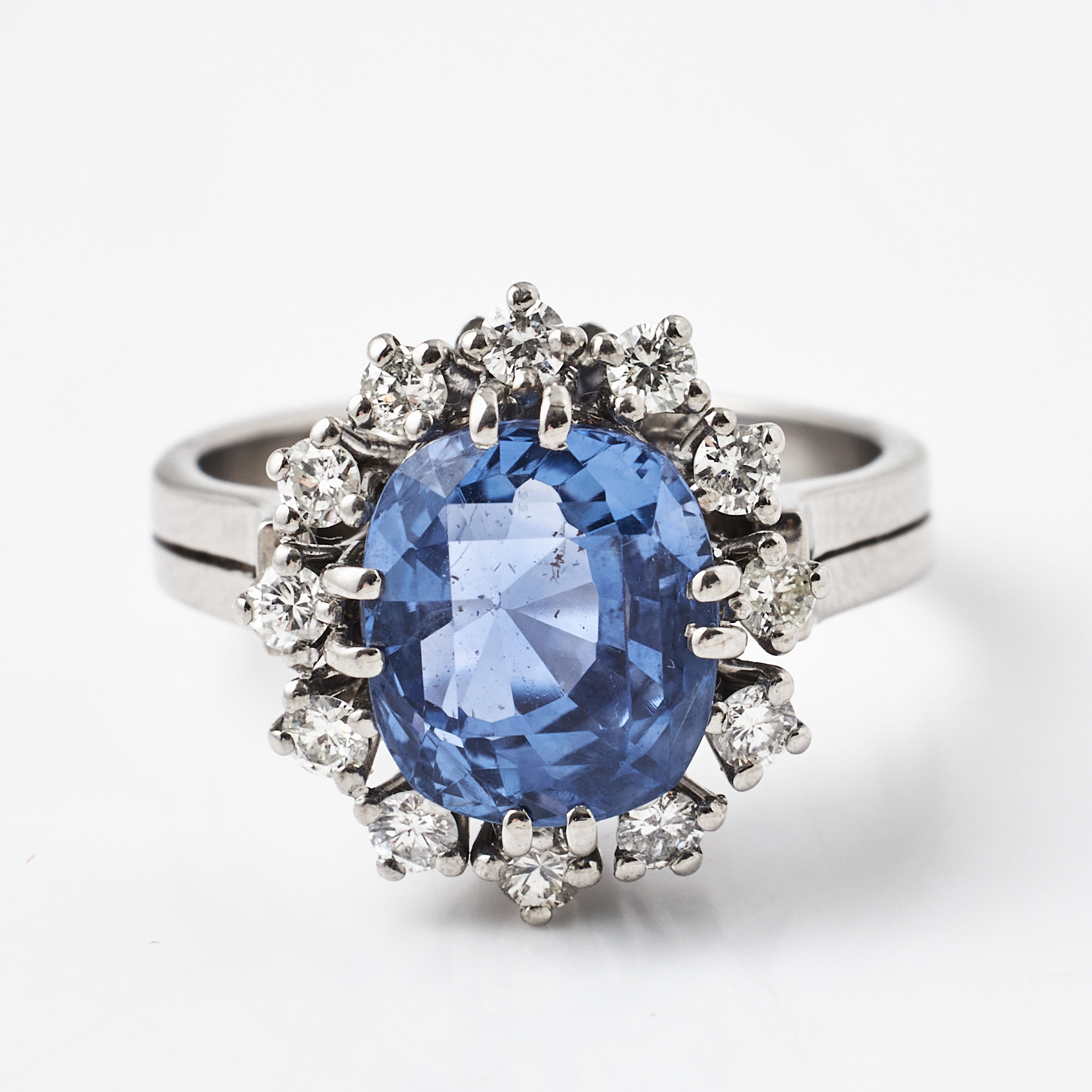 RING, 18 k vitguld, fantasislipad ljusblå safir ca 4,50 ct, bekransad av 12 briljanter totalt ca 0,48 ct., spår av otydliga utländska stämplar.