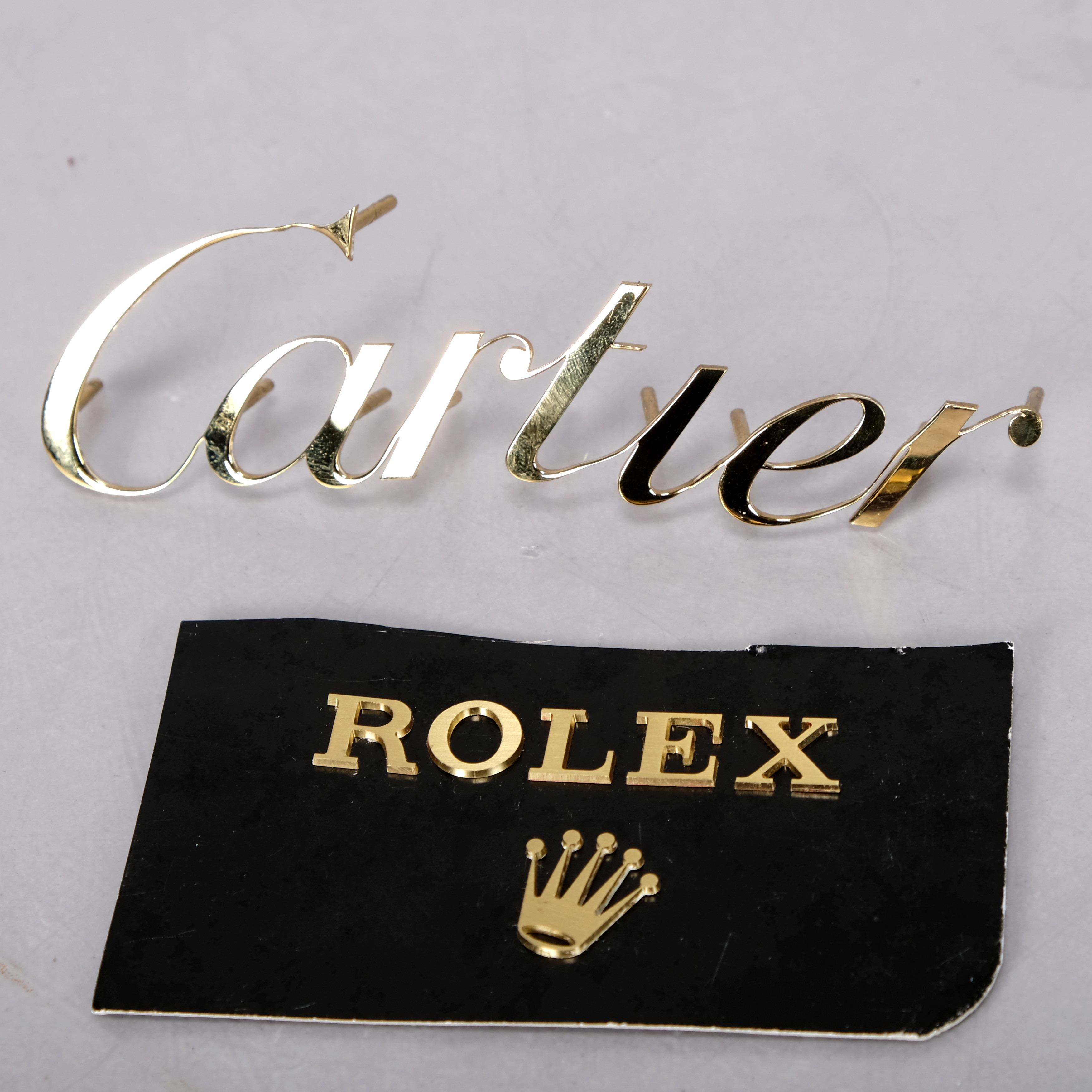 CARTIER OCH ROLEX, emblem, mässing, (2 delar.