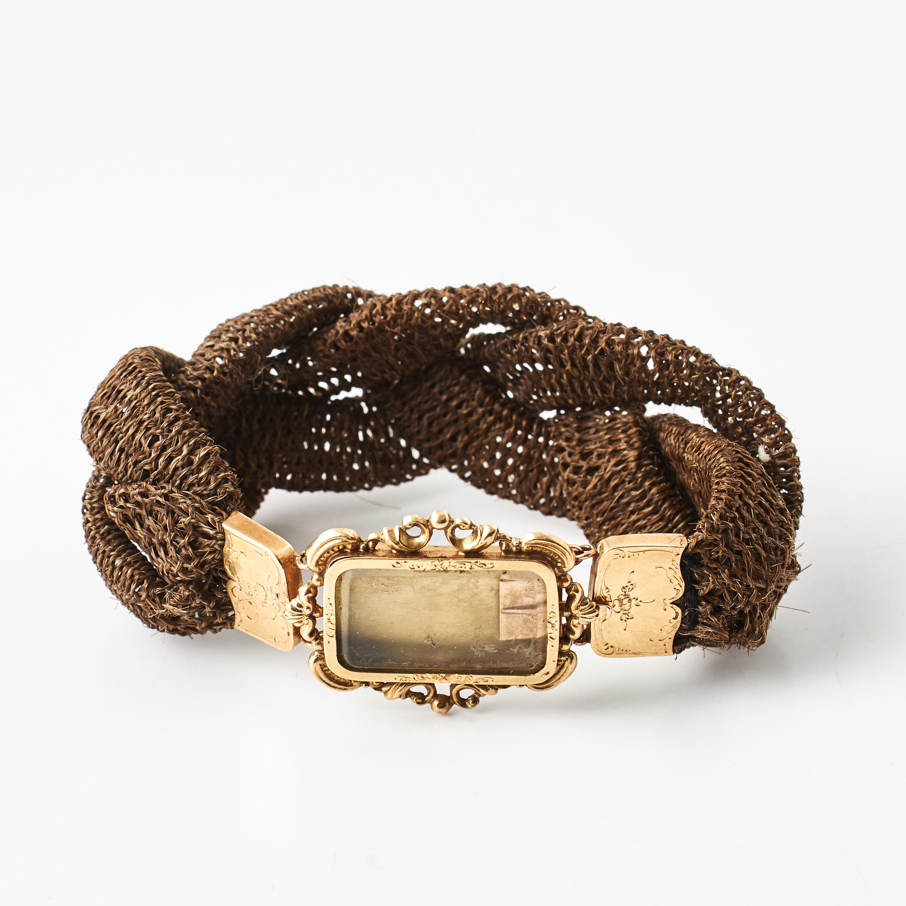 ARMBAND, flätat hårarbete, mittparti med öppningsbar gömma, 18 k guld, graverad dekor av rocailler och akantusslingor, 1800-talets senare del.