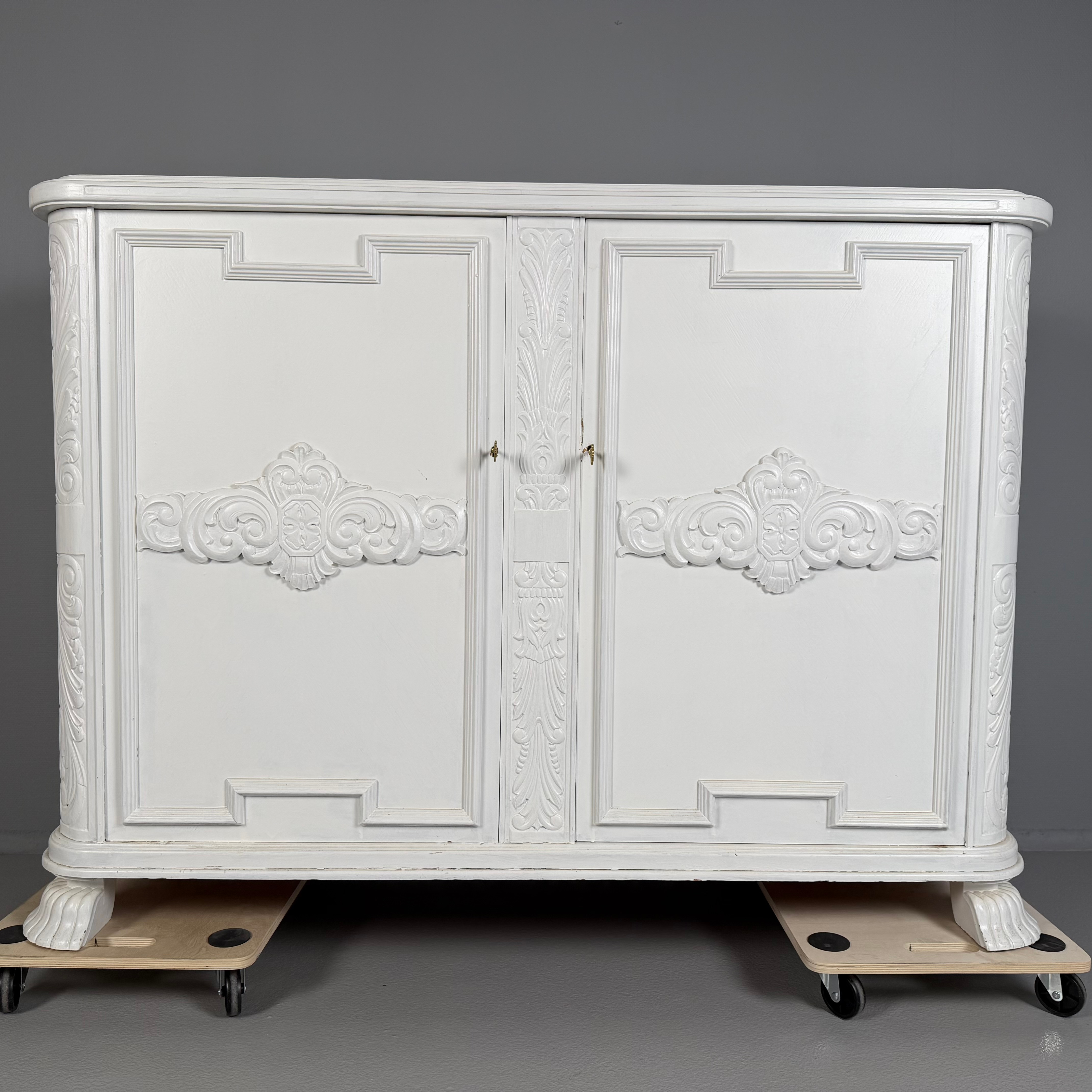 SKÄNK, 1920/30-tal, tjugotalsklassicism/barockstil, vitbemålad, ovandel med profilerad kant, dörrluckor med dekor lister samt träskuren dekor av stiliserad blomster, invändig inredning med lådor, stiliserade tassfötter.
