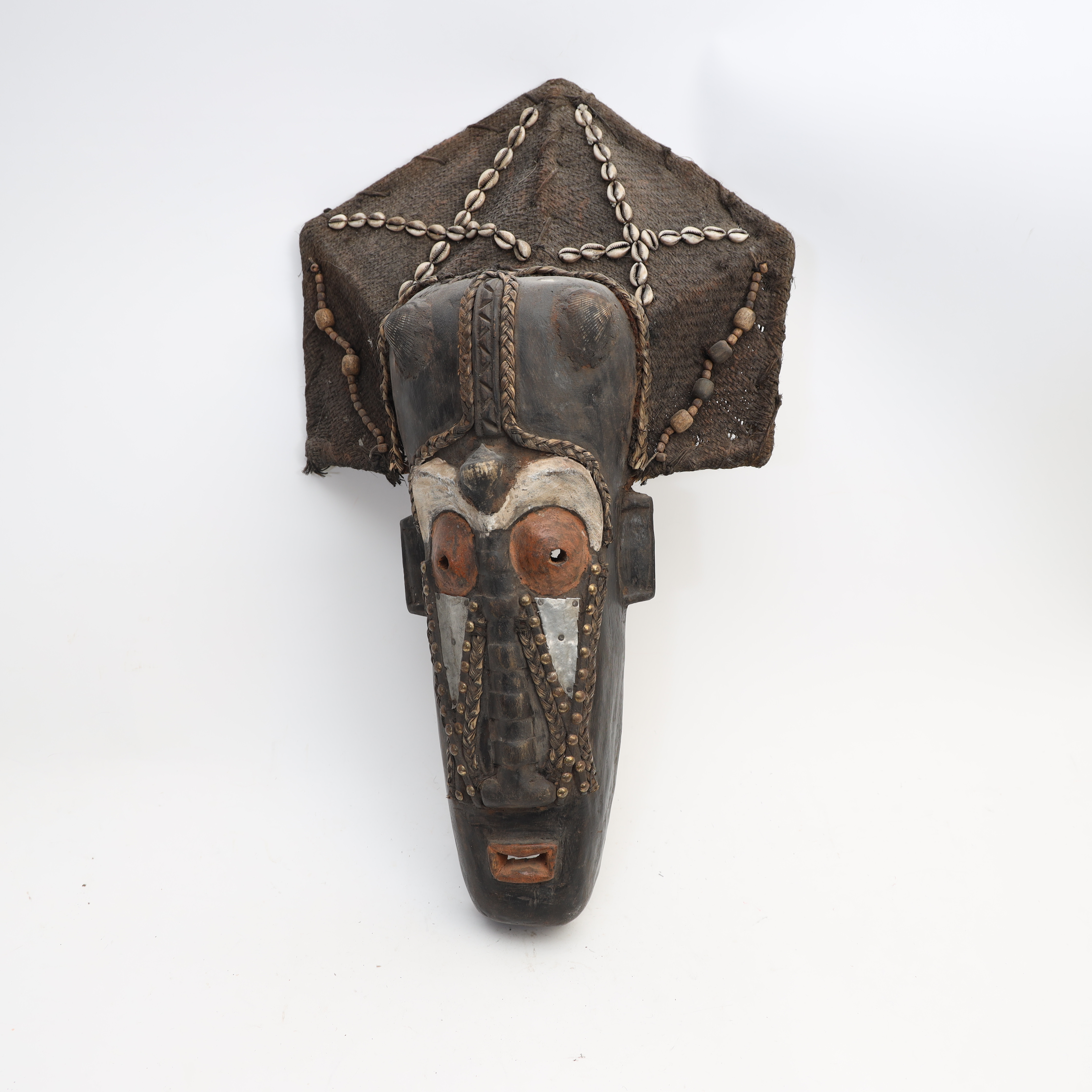 MASK, Afrika, skuret och bemålat trä, med snäckor och mässingsnitar, samt textil. Troligen tidigt 1900-tal.