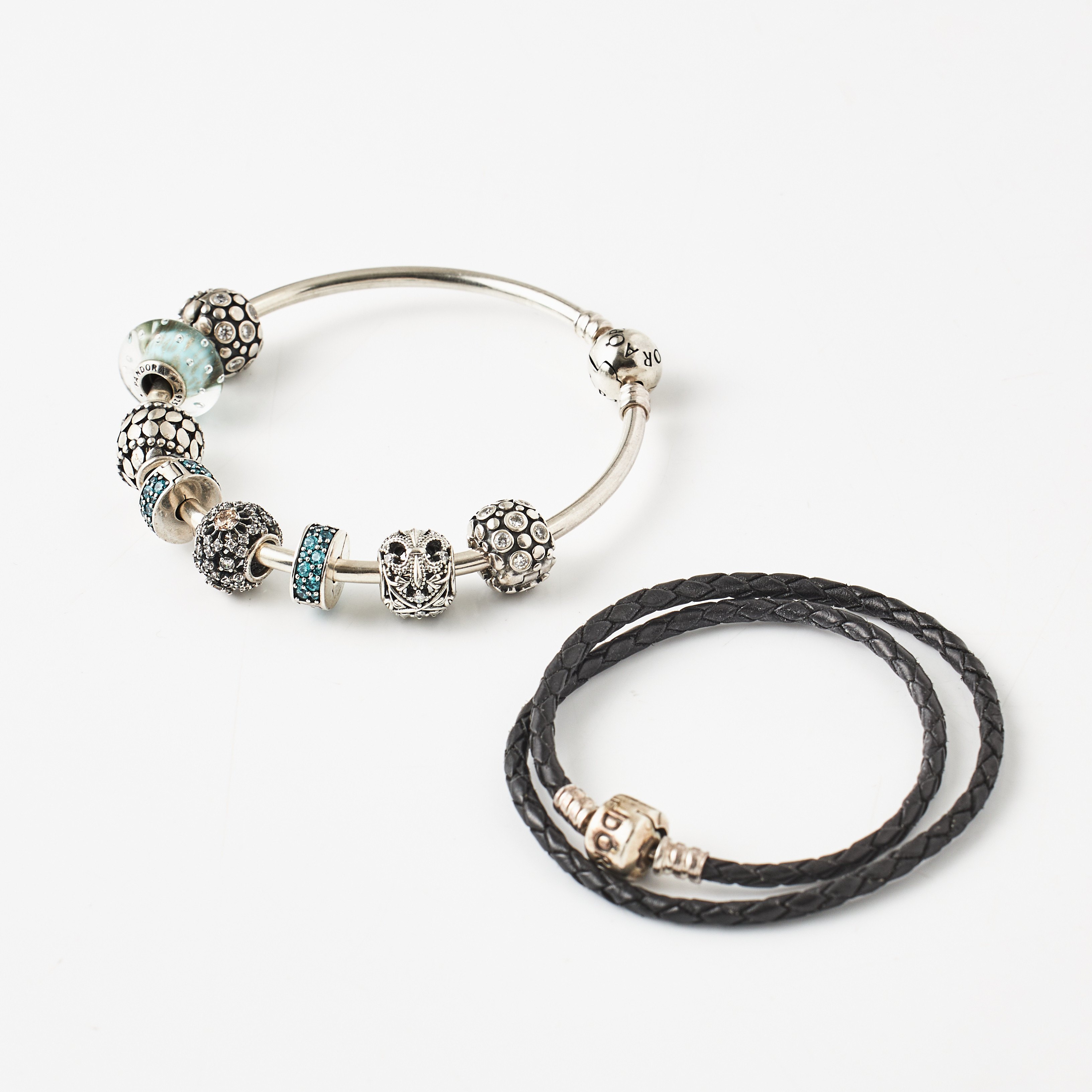 PANDORA, armband, virad lädersnodd, avslut i form av dobbar, låsdel samt detaljer i sterlingsilver, armring med 8 berlocker, sterlingsilver, bl a berlocker med fasettslipade vita stenar, en diskformad av turkost glas.