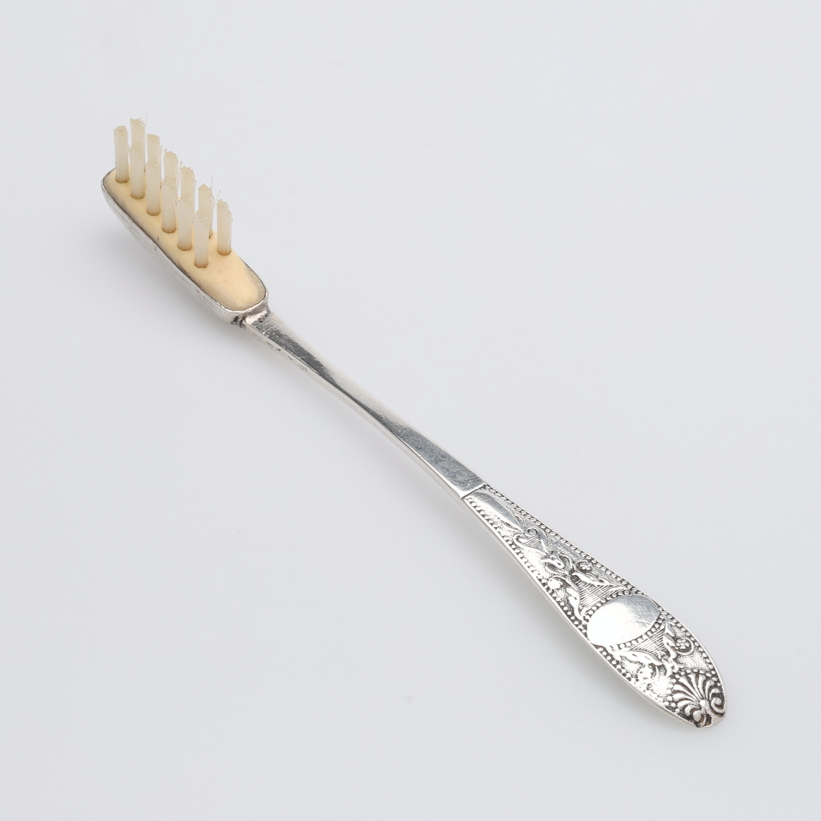 EN ELEGANT TANDBORSTE AV GUSTAF FOLCKER, silver och senare tillkommet polymert material, snäckmodell, tillverkad i Stockholm året 1843.