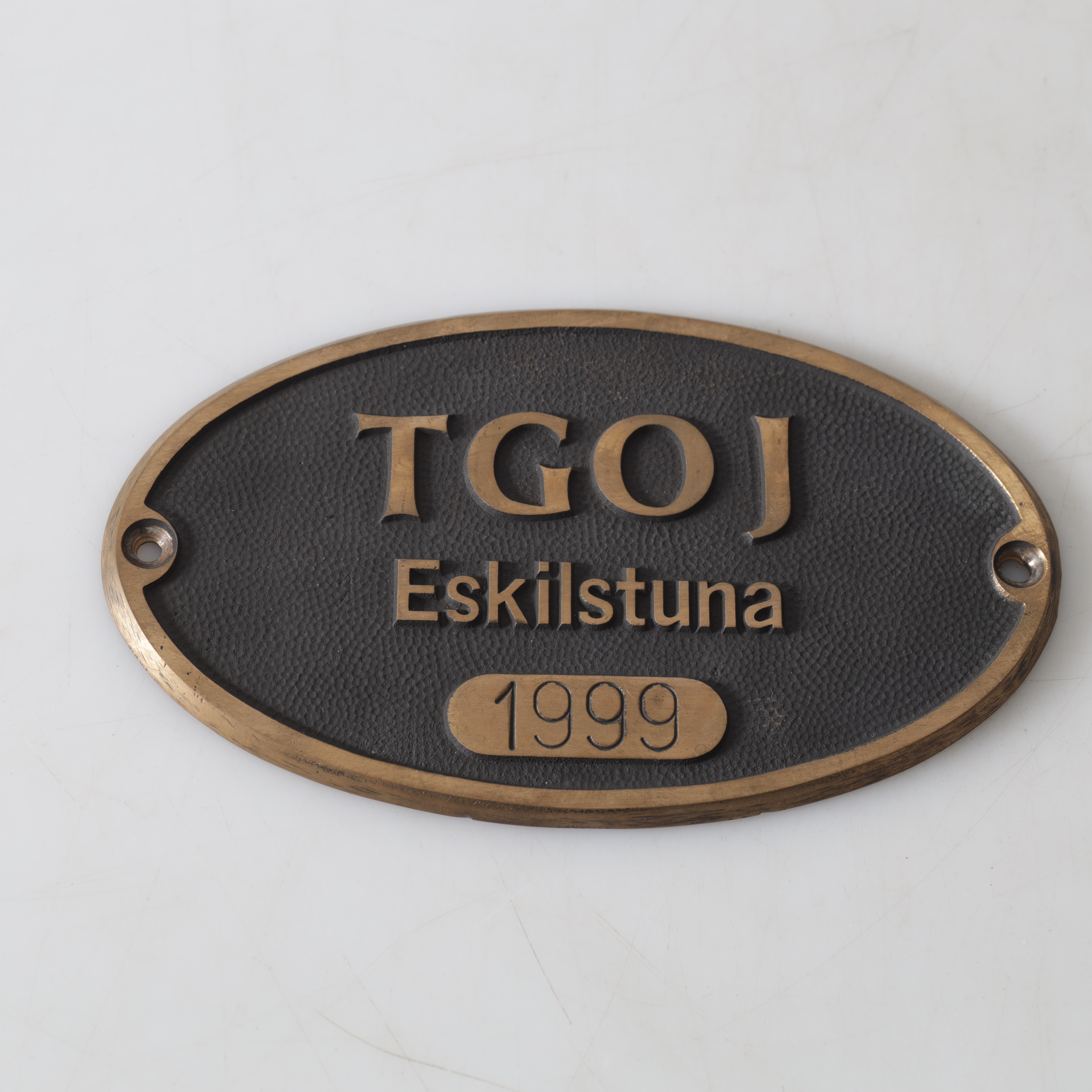 SKYLT, mässing, TGOJ, Trafikaktiebolaget Grängesberg–Oxelösunds Järnvägar, Eskilstuna, 1999.